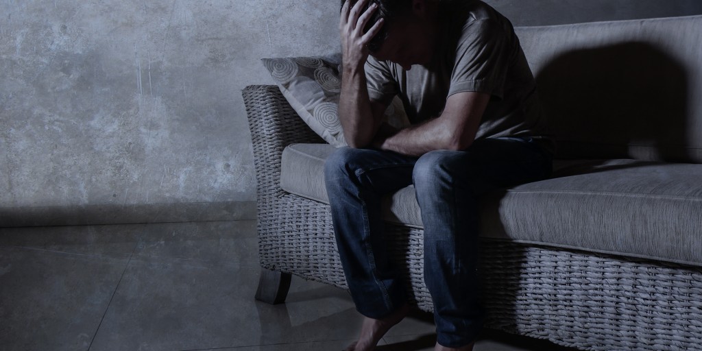 depressed man despairing while sitting on couch