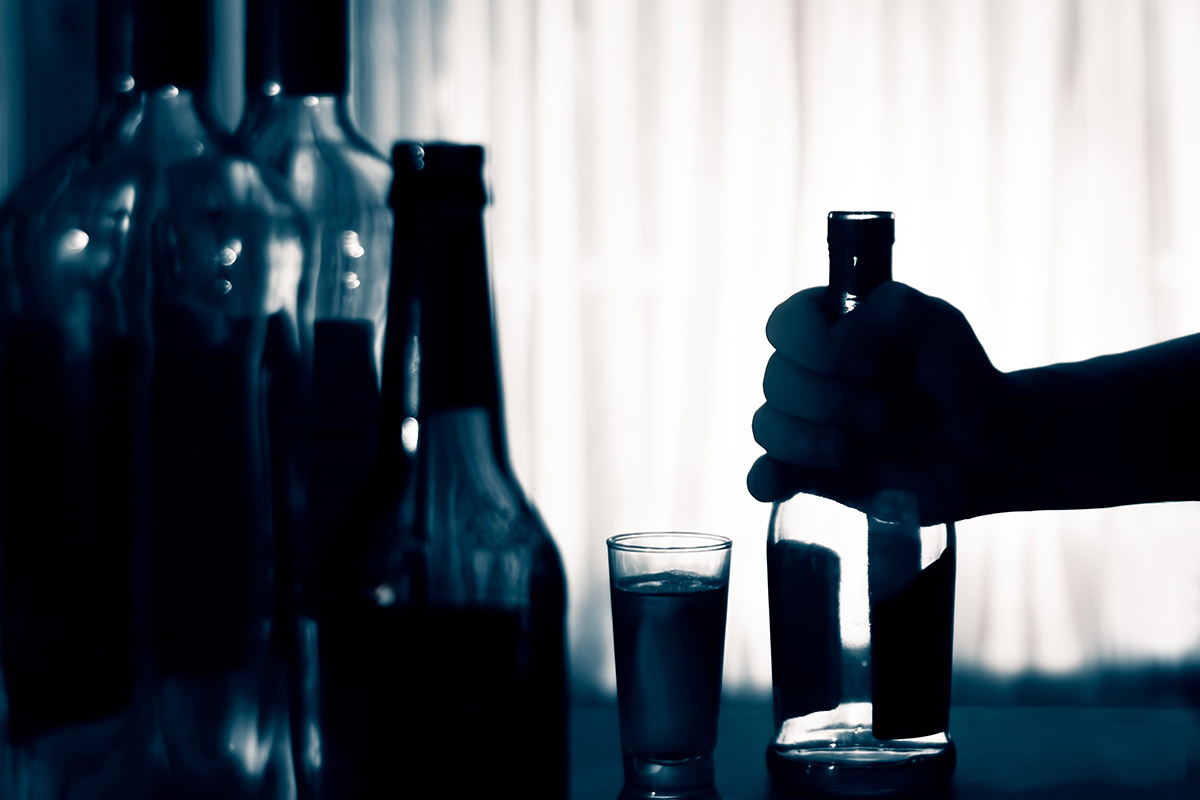 a man grasps a bottle and thinks about the signs of alcoholism