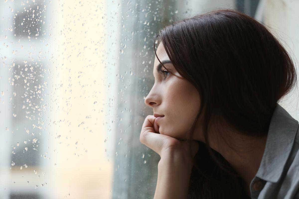 a woman stares out the window as she struggles to maintain sobriety on a rainy day